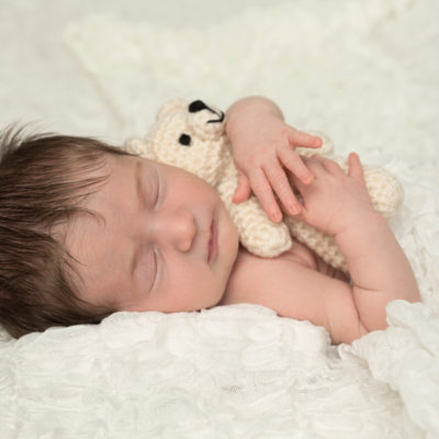 Newborn with dark hair holding teddy